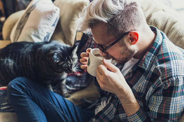 muž popíjející kávu a kočka na pohovce